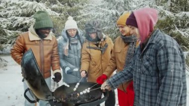 Bir grup neşeli çoklu etnik arkadaş kış günü ormanda barbekü ateşinde lokum kızartıyorlar.
