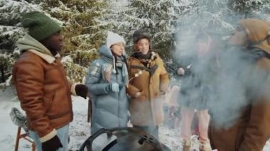 Ormanda barbekü yapan ve kış pikniğinde kızarmış marşmelov yiyen çok ırklı arkadaşlar.