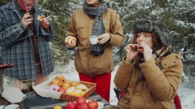 Genç arkadaşlar, kış ormanlarındaki kamp alanında yemek yerken ızgara yemek yiyip sohbet ediyorlar.