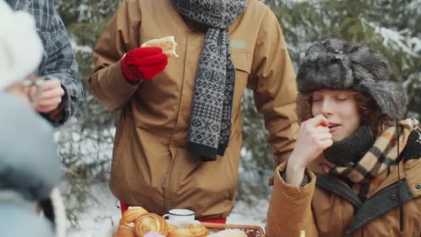 年轻而积极的朋友在冬季森林的餐桌边吃饭和说话 同时在营地吃饭 — 图库视频影像