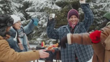 Kış ormanlarında kamp alanında gülümseyen ve dans eden mutlu çok ırklı genç arkadaşlar.