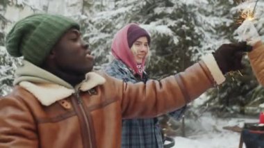 Kış ormanlarında Noel 'i dışarıda kutlarken ellerinde maytap tutan ve daireler çizen neşeli çoklu etnik arkadaşlar.