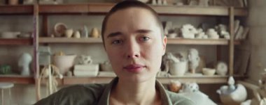 Genç bayan çömlekçinin atölyede poz verirken kameraya bakışının göğüs portresi.