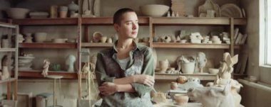 Lekeli önlüklü, çömlek atölyesinde kameraya poz veren genç bir kadının portre fotoğrafını yakınlaştır.