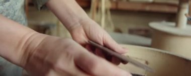 Kadın çömlekçinin yakın çekimleri, atölyede kille çalışmak için tahta kaburga seçiyor.