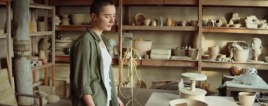 Genç bayan çömlekçi atölyede yürüyor, önlüğünü giyiyor ve işe hazırlanıyor.