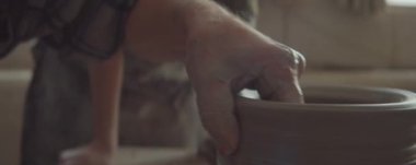 Kıdemli çömlekçinin dönme dolapta kil kaseyi şekillendirdiği ve kız öğrenciye bir şeyler söylediği yakın çekim.