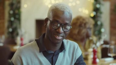 Genç Afrikalı Amerikalı bir adam kafede oturuyor, birini dinliyor ve telefon kullanıyor.