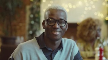 Kafede oturan, kameraya bakıp gülümseyen Afro-Amerikan bir adamın portresi.