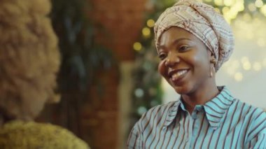 Kafede durmuş sevgilisiyle sohbet eden kafası sarılı güzel Afro-Amerikan bir kadının omzunun üstünden.