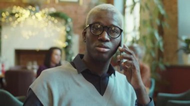 Kafede cep telefonuyla konuşan gözlüklü genç Afro-Amerikan işadamının göğüs yukarı çekimi.