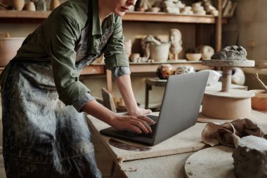 Craftsperson atölyede dizüstü bilgisayarda çalışıyor.