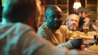 Modern gastropub 'da bir grup adam birlikte oturup gevşeyip, bira içiyor, abur cubur yiyor ve sohbet ediyor.