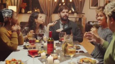 Bir grup modern genç arkadaş doğum günü partisinde yemek masasında oturmuş şapka oyunu oynuyorlar.