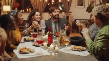 Bir grup çok ırklı genç arkadaş doğum günü partisinde yemek masasında oturmuş şapka oyunu oynuyorlar.