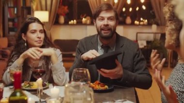 Bir grup modern çoklu etnik arkadaş yemek masasında oturup kelime tahmin oyunu oynayarak eğleniyorlar.