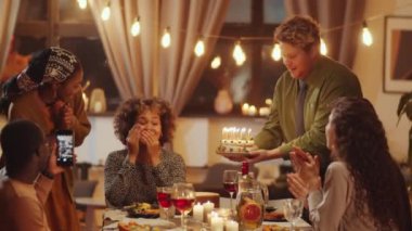 Mutlu genç siyahi kadın arkadaşlarıyla doğum gününü kutluyor, dilek diliyor ve doğum günü pastası mumlarını üflüyor.