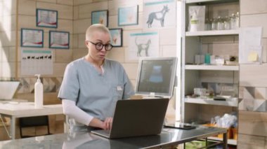 Female veterinarian in medical uniform talking on online video call on laptop during workday in clinic
