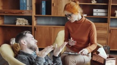 Depresyondaki adam danışmanlık ofisinde kanepede uzanıyor, ağlıyor ve şefkatli kadın psikologla sorunları tartışıyor.