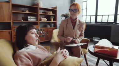 Genç mutsuz kadın kanepeye uzanıyor, yastığa sarılıyor ve terapi sırasında sorunlarını ve duygularını kadın psikoloğa anlatıyor.