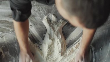 Erkek şefin un yığınlarını üst üste yığmasının ve hamuru hazırlarken masanın ortasına iyi yerleştirmesinin üst üste çekimleri.