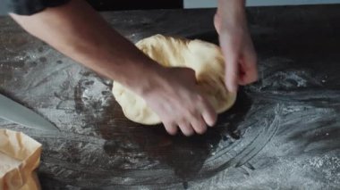 Erkek aşçının un kaplı ahşap mutfak masasında hamur yoğurmasını yakından çek.