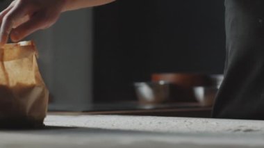 Erkek aşçının kağıt torbadan un atıp masaya serptiği yakın plan çekimleri.