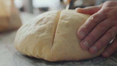 Erkek fırıncının hamur yoğurdunu bıçakla keserken ve parçalarken yakın plan çekimleri.