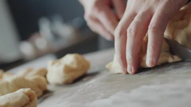 Hollanda açılı erkek fırıncının eli yakın çekimde hamuru bıçakla parçalara ayırıyor.