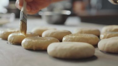 Hamburgerleri fırında pişirmeden önce fırında yumurta fırçalayan fırıncının yakın çekimi.