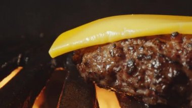 Izgarada ve ateşte pişerken hamburger etinin üzerinde eriyen peynirin aşırı yakın plan çekimi.