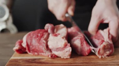 Tahtada bıçakla çiğ et kesen tanınmayan bir adamın ellerini yakın plan çek.