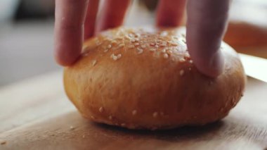 Erkek ellerinin susamlı ekmeği bıçakla ikiye böldüğü yakın çekim.