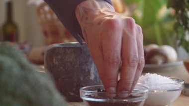 Erkek aşçının elini kaldırıp cam kaseden bir tutam karabiber alıp taş havan topuna döküyoruz.