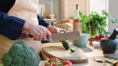 Önlüklü erkek aşçının, mutfakta yemek pişirirken kasap bıçağıyla salatalık keserken orta bölüm fotoğrafı.