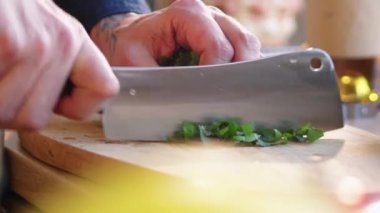 Mutfak masasında yemek pişirirken kasap bıçağıyla maydanoz doğrayan erkek şefin yakın plan fotoğrafları.