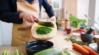 Mutfakta yemek pişirirken maydanozu odun kesme tahtasını bıçakla keserken önlüklü profesyonel aşçının fotoğrafını yakınlaştır.