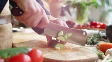 Erkek aşçının ahşap kesme tahtasının üzerinde salatalık keserken ve kasap bıçağının kılıcındaki parçaları keserken yakın plan çekimleri.