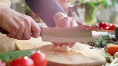 Erkek aşçının apronlu, tahta kesme tahtasındaki çiğ şampiyonları kasap bıçağıyla doğradığı yakın çekim.