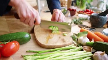 Erkek şefin ahşap kesme tahtasıyla salatalık keserken ve restoran mutfağında yemek pişirirken bıçaktan parçaları çıkarırken görüntüyü yakınlaştır.