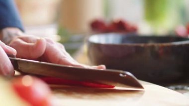 Erkek aşçının ahşap tahtada kırmızı biber keserken ve hamuru bıçakla keserken yakın plan çekimleri.