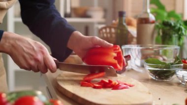 Mutfakta yemek pişirirken tahta tahtada kırmızı dolma biber kesen erkek şefin yakın çekim görüntüsü.