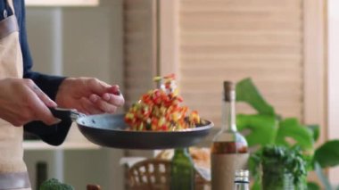 Lokanta mutfağında yemek pişirirken önlüklü, sebzeleri tavaya fırlatan tanınmamış bir erkek şefin yavaş çekim çekimi.