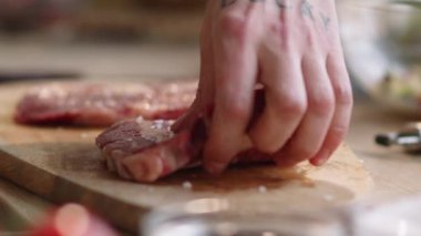 Erkek ellerinin çiğ et bifteğinin üzerine tuz dökmesini ve sonra ahşap kesim tahtasının üzerine çevirerek pişirmeye hazırlanmasını yakından izleyin.