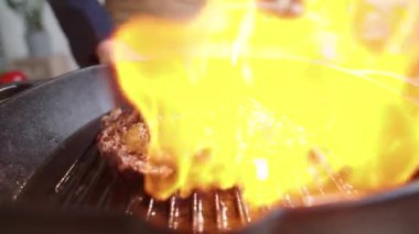 Profesyonel şefin yakın plan çekimleri, şömineyi tutuşturmak için çakmak kullanması ve sonra et bifteği yakıp maşayla çevirmesi.