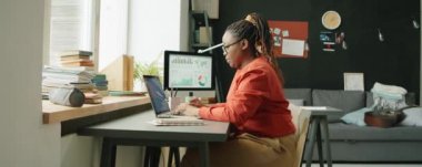 Genç Afrikalı Amerikalı kadının laptopta yazarken ve evde çalışırken notlar alırken görüntüsünü yakınlaştır.