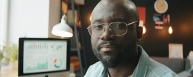 Gözlüklü Afro-Amerikan bir adamın merkez büroda çalışırken kameraya poz verirken çekilen portresi.