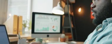 Afro-Amerikalı adamın kablosuz kulaklık takıp müzik dinlerken ve bilgisayarla çalışırken görüntüsünü kaldır.