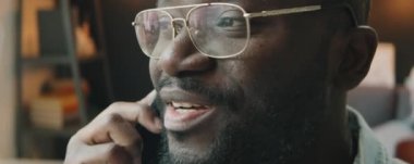 Gözlüklü Afrikalı Amerikalı adamın cep telefonuyla bir şey tartışırken yakın plan çekimleri.