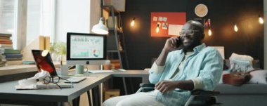 Tekerlekli sandalyede oturan ve merkez büroda çalışırken cep telefonuyla konuşan Afrikalı Amerikalı iş adamı.